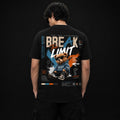 A man viewed from behind wearing a black short-sleeve t-shirt with a large graphic print on the back. The graphic features the text 'BREAK THE LIMIT' in white and orange, a cartoon teddy bear in a denim jacket and sunglasses, and blue and orange paint splatter details, set against a dark studio background.