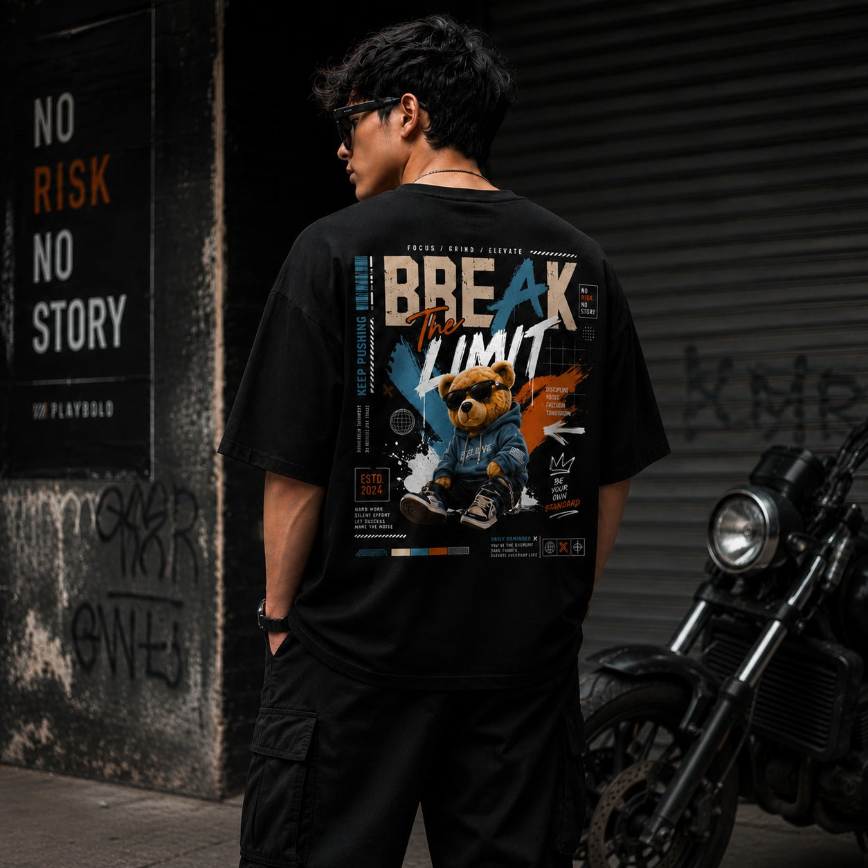 Person wearing a black t-shirt with a graphic design, standing next to a motorcycle in an urban setting.